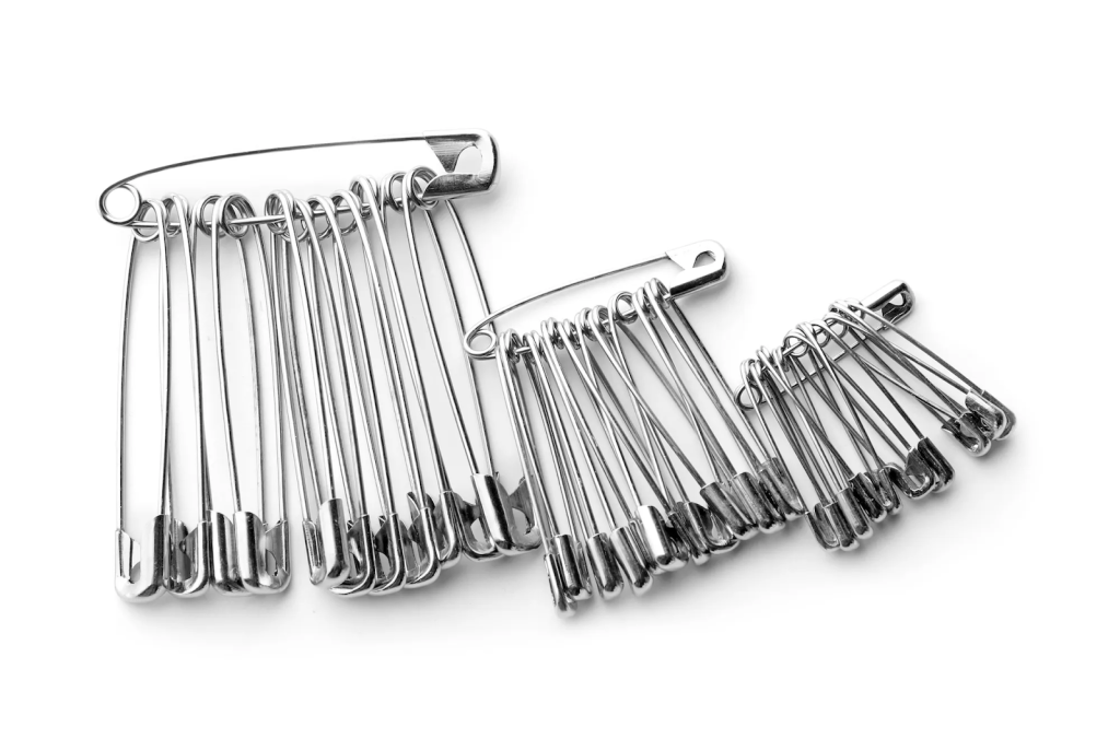 Three sets of silver safety pins grouped by size, arranged on a white background—essential tools for any unexpected wardrobe mishap.
